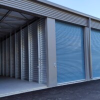 A row of drive-up storage units with blue doors. The farthest left unit is open.